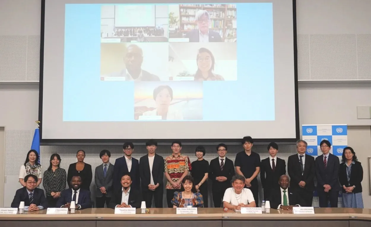 Students, judges and guests in a group photograph at the United Nations University in Tokyo, with online participants on the screen behind them.